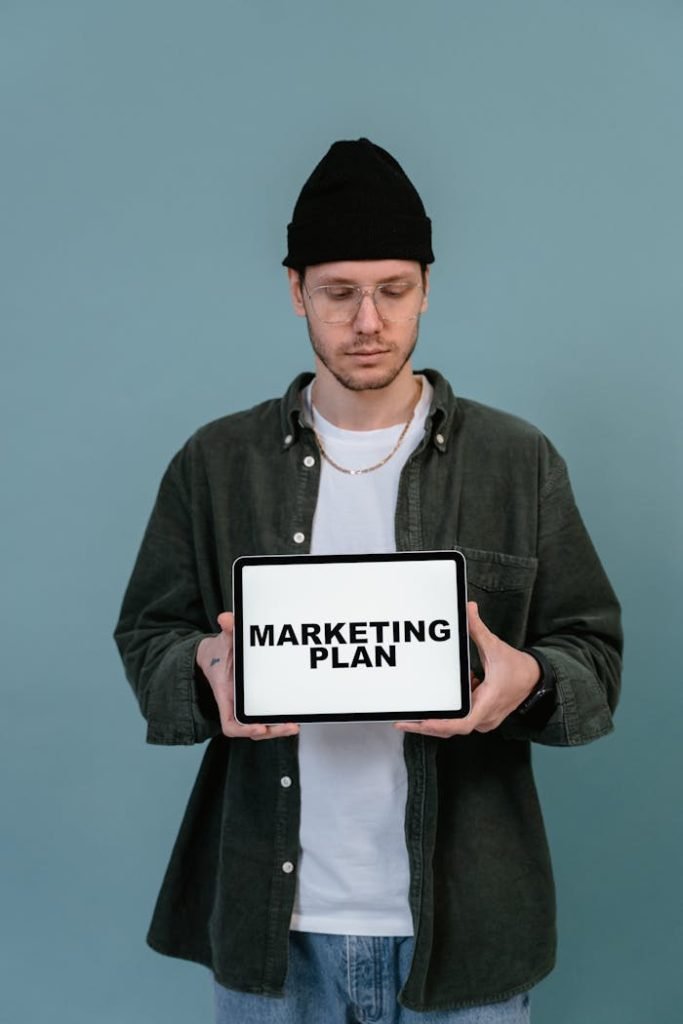 Adult wearing casual clothing holding a tablet that reads Marketing Plan.
